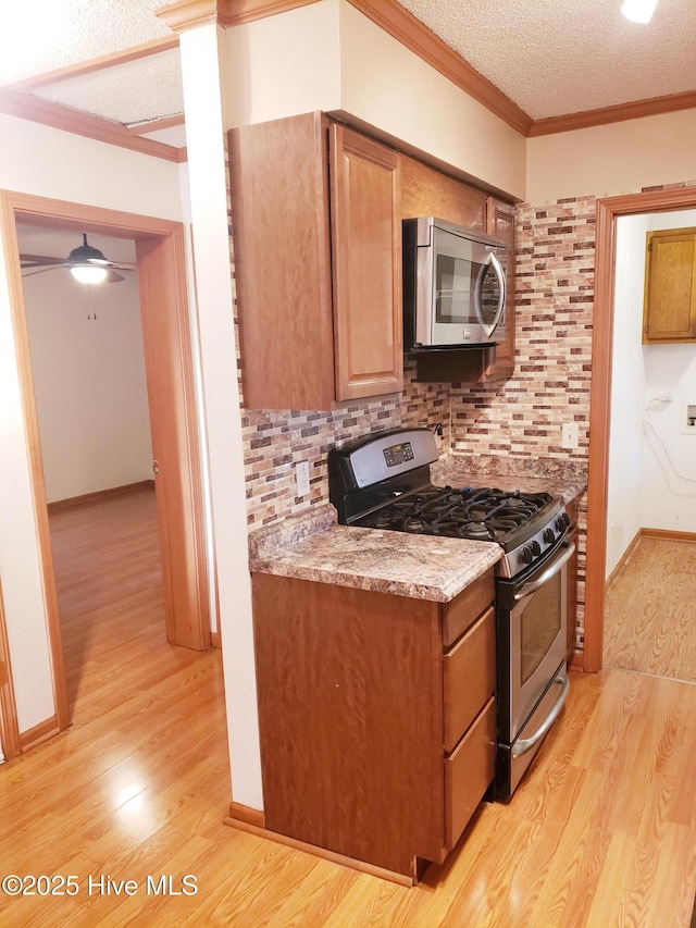 kitchen featuring a textured ceiling, backsplash, light wood-type flooring, and stainless steel appliances