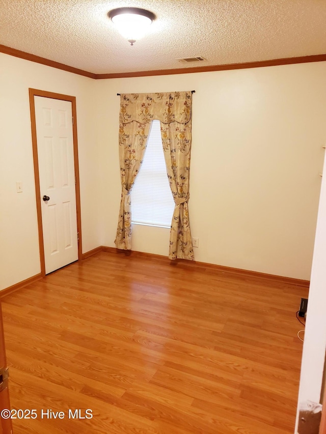 empty room featuring wood-type flooring, a textured ceiling, and ornamental molding