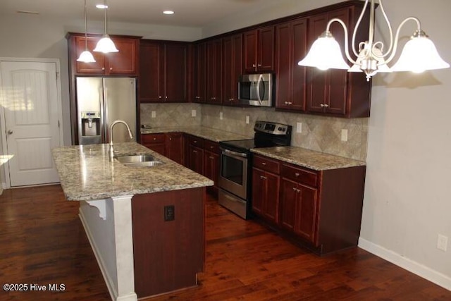 kitchen with sink, light stone counters, decorative light fixtures, a center island with sink, and appliances with stainless steel finishes