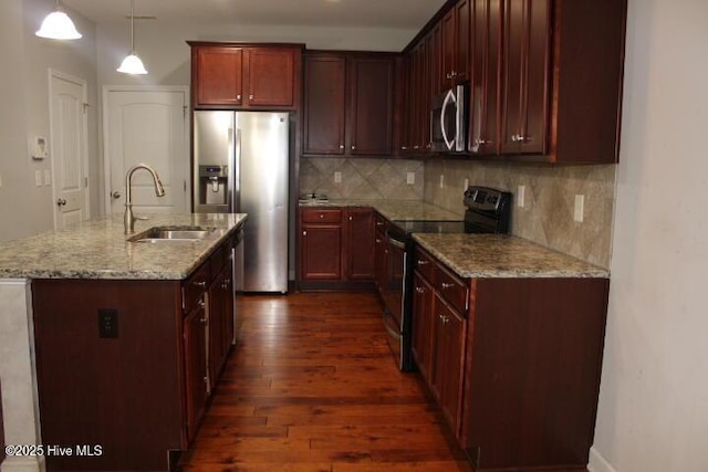 kitchen with sink, dark wood-type flooring, light stone counters, a kitchen island with sink, and appliances with stainless steel finishes