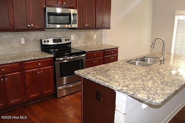 kitchen featuring light stone countertops, appliances with stainless steel finishes, dark wood-type flooring, and sink