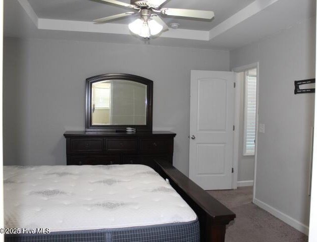 carpeted bedroom with a tray ceiling and ceiling fan