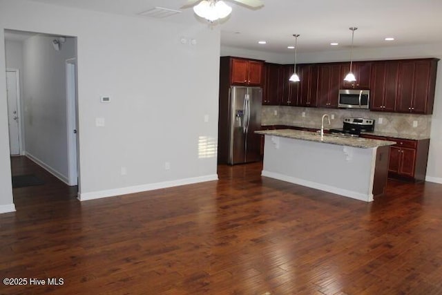 kitchen with tasteful backsplash, stainless steel appliances, decorative light fixtures, a breakfast bar area, and an island with sink