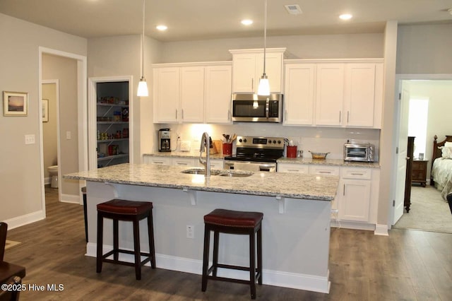 kitchen with dark hardwood / wood-style flooring, pendant lighting, a center island with sink, white cabinets, and appliances with stainless steel finishes