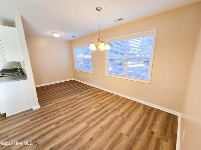 unfurnished dining area featuring sink, hardwood / wood-style floors, and a notable chandelier