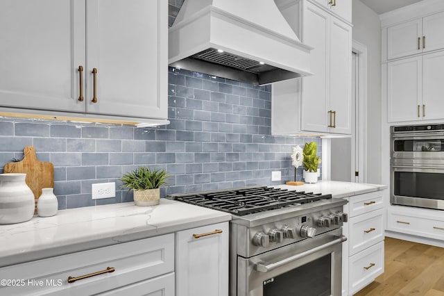 kitchen featuring premium range hood, stainless steel appliances, light stone counters, tasteful backsplash, and white cabinets