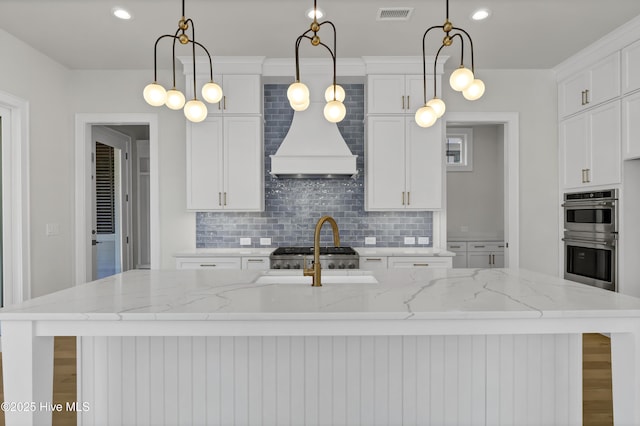 kitchen with light stone counters, decorative light fixtures, and a center island with sink