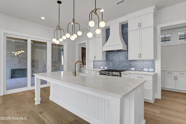 kitchen featuring white cabinetry, premium range hood, sink, and a kitchen island with sink