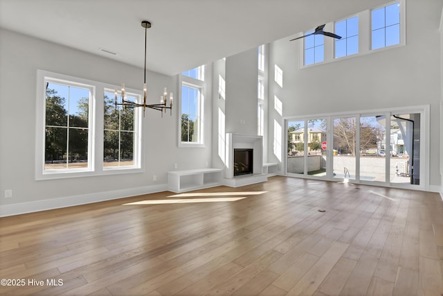 unfurnished living room with a notable chandelier, a towering ceiling, and light hardwood / wood-style flooring