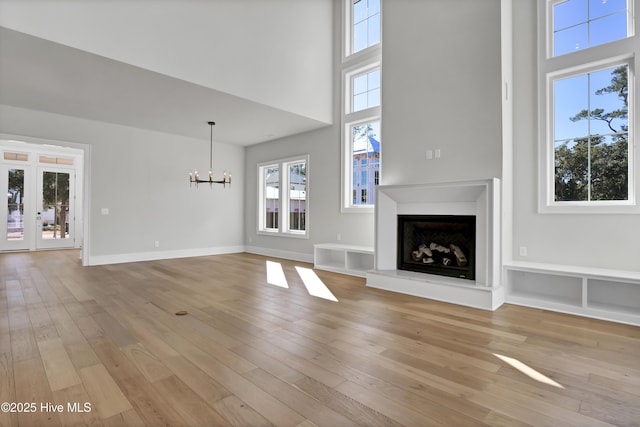 unfurnished living room featuring french doors, a towering ceiling, light hardwood / wood-style flooring, and a notable chandelier