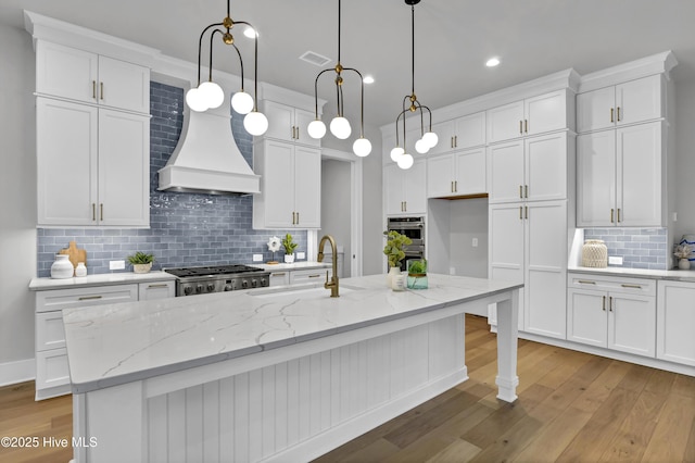 kitchen featuring white cabinetry, hanging light fixtures, and an island with sink