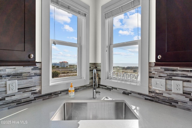 kitchen with a sink, tasteful backsplash, dark brown cabinets, and light countertops