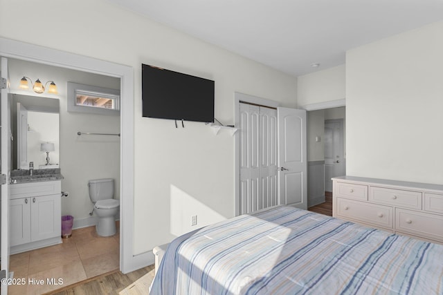 bedroom with baseboards, light wood finished floors, ensuite bath, a sink, and a closet