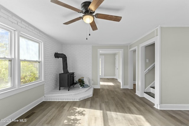 unfurnished living room featuring ceiling fan, wood-type flooring, a wood stove, and brick wall