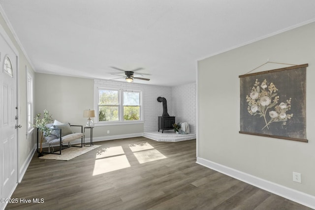 unfurnished room with ceiling fan, a wood stove, dark wood-type flooring, and ornamental molding