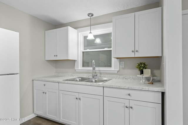 kitchen featuring white fridge, white cabinetry, hanging light fixtures, and sink