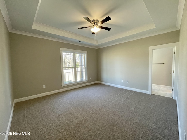 empty room with carpet floors, a tray ceiling, ceiling fan, and ornamental molding