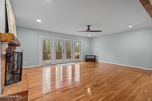 unfurnished living room with ceiling fan, french doors, light wood-type flooring, and a brick fireplace