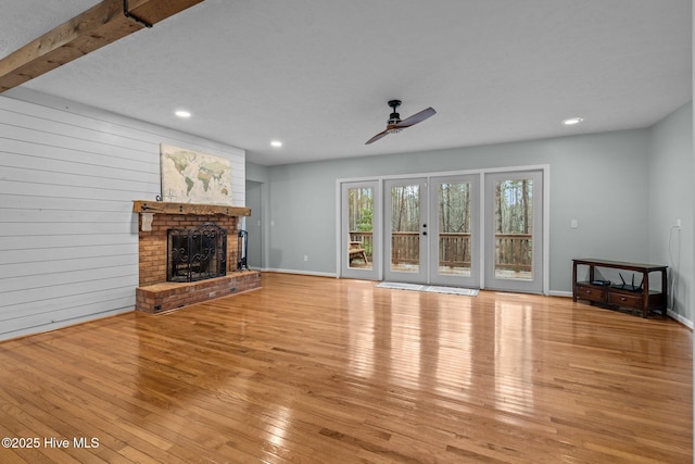 unfurnished living room featuring ceiling fan, wooden walls, light hardwood / wood-style flooring, beamed ceiling, and a fireplace