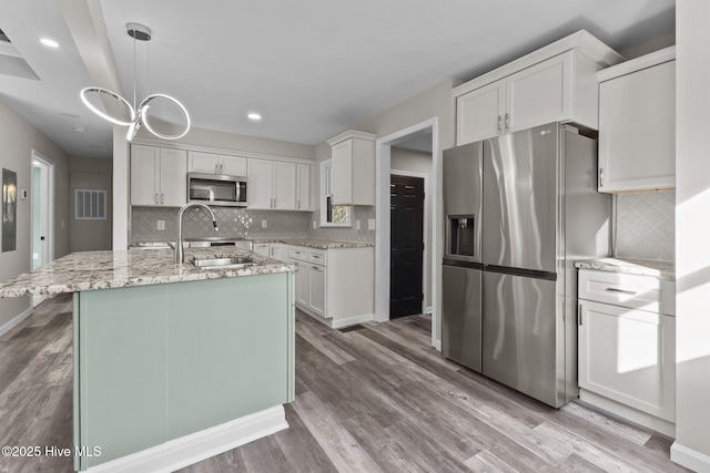 kitchen featuring appliances with stainless steel finishes, sink, a center island with sink, decorative light fixtures, and white cabinetry