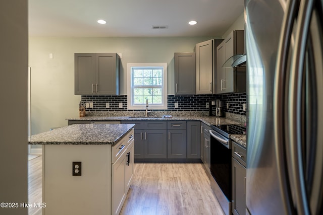 kitchen featuring a center island, dark stone counters, wall chimney range hood, sink, and appliances with stainless steel finishes