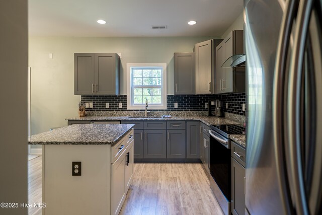 kitchen with stainless steel range with electric stovetop, gray cabinetry, wall chimney range hood, and light stone counters