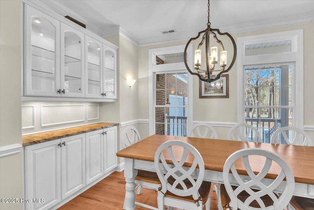 dining area with light hardwood / wood-style floors, ornamental molding, and a notable chandelier