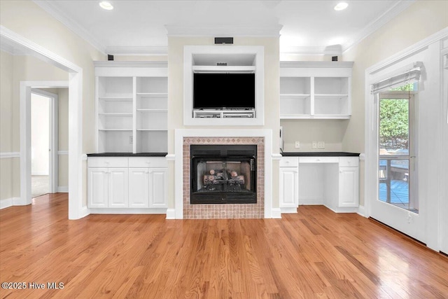 unfurnished living room featuring a tiled fireplace, crown molding, and light hardwood / wood-style flooring