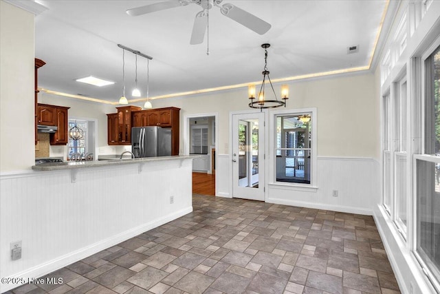 kitchen featuring stainless steel refrigerator with ice dispenser, kitchen peninsula, pendant lighting, ceiling fan with notable chandelier, and ornamental molding