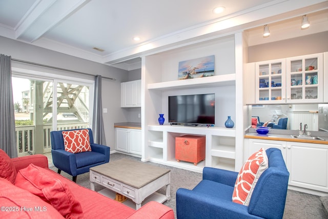 carpeted living room with beamed ceiling, ornamental molding, sink, and built in features