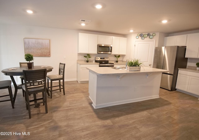 kitchen featuring appliances with stainless steel finishes, white cabinetry, and an island with sink