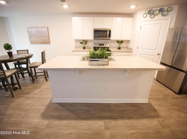 kitchen with a breakfast bar, stainless steel appliances, light hardwood / wood-style flooring, white cabinets, and an island with sink