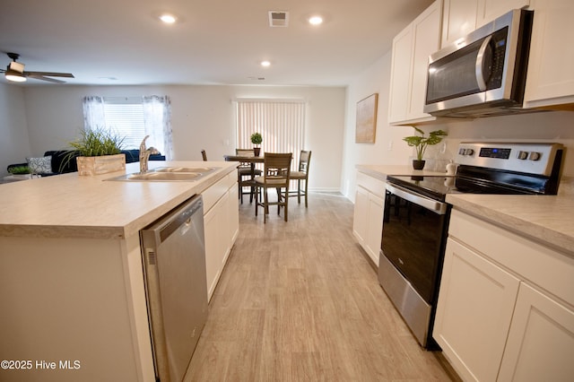 kitchen with stainless steel appliances, sink, light hardwood / wood-style floors, white cabinetry, and an island with sink