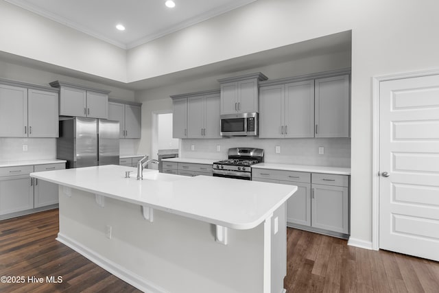 kitchen with stainless steel appliances, a kitchen island with sink, gray cabinets, and a kitchen bar