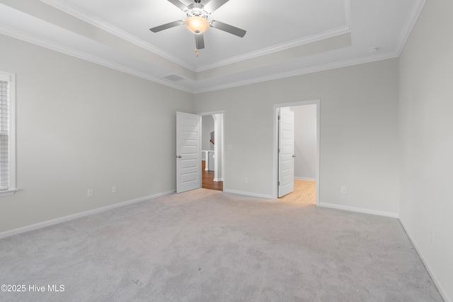 unfurnished bedroom with a spacious closet, a raised ceiling, crown molding, ceiling fan, and light carpet