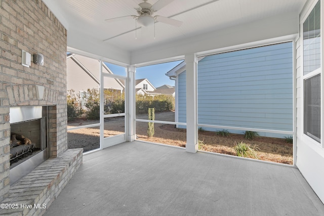 unfurnished sunroom featuring an outdoor brick fireplace and ceiling fan