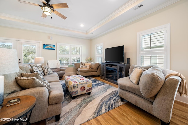 living room featuring ceiling fan, ornamental molding, wood-type flooring, and a tray ceiling