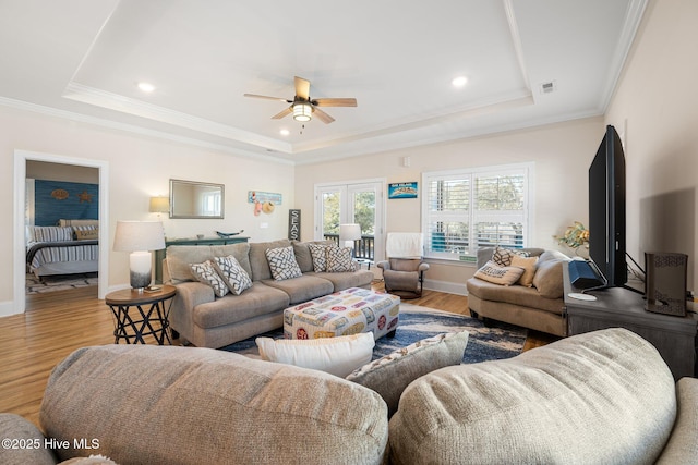 living room featuring ceiling fan, ornamental molding, a tray ceiling, and hardwood / wood-style floors