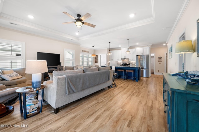 living room with ceiling fan, ornamental molding, a raised ceiling, and light wood-type flooring