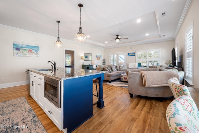 kitchen with sink, an island with sink, stainless steel appliances, light stone countertops, and white cabinets