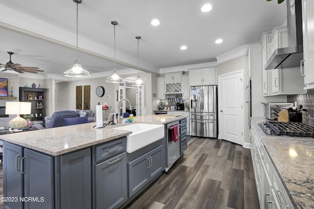 kitchen with wall chimney exhaust hood, stainless steel appliances, tasteful backsplash, a center island with sink, and white cabinets