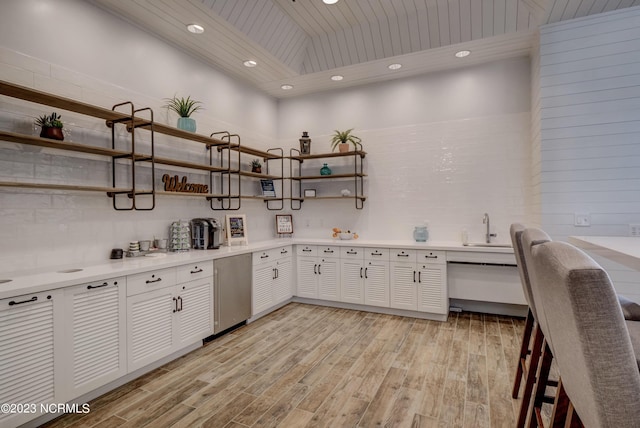 kitchen featuring a towering ceiling, sink, light hardwood / wood-style flooring, wooden ceiling, and white cabinetry