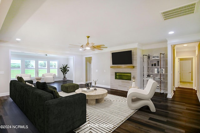 living room featuring ceiling fan, crown molding, a fireplace, and dark wood-type flooring