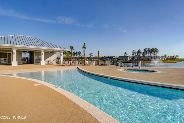 view of swimming pool featuring a water view, a patio, and a hot tub