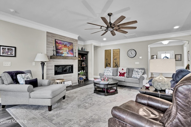 living room featuring ceiling fan, wood-type flooring, ornamental molding, and a tile fireplace