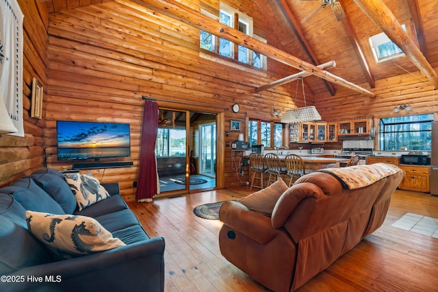 living room with rustic walls, ceiling fan, high vaulted ceiling, and a skylight