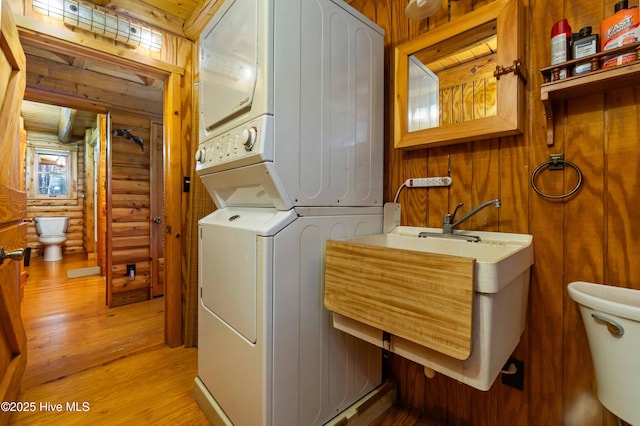 laundry room with light hardwood / wood-style floors, stacked washer and dryer, and rustic walls