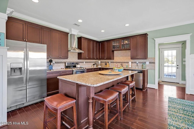 kitchen with stainless steel appliances, a kitchen bar, crown molding, and wall chimney exhaust hood