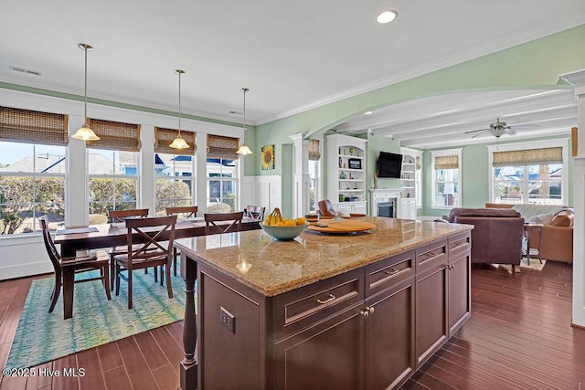 kitchen with ceiling fan, dark hardwood / wood-style flooring, ornamental molding, a kitchen island, and decorative light fixtures