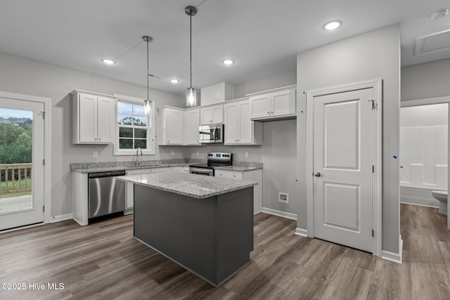 kitchen featuring appliances with stainless steel finishes, light stone counters, pendant lighting, white cabinets, and a center island